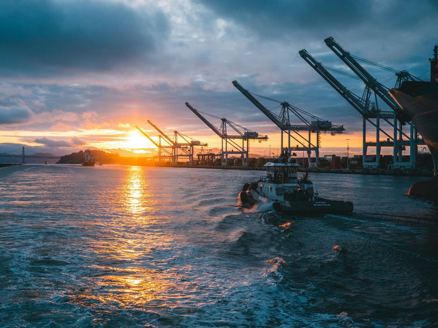 Tug boat passing container cranes at sunset